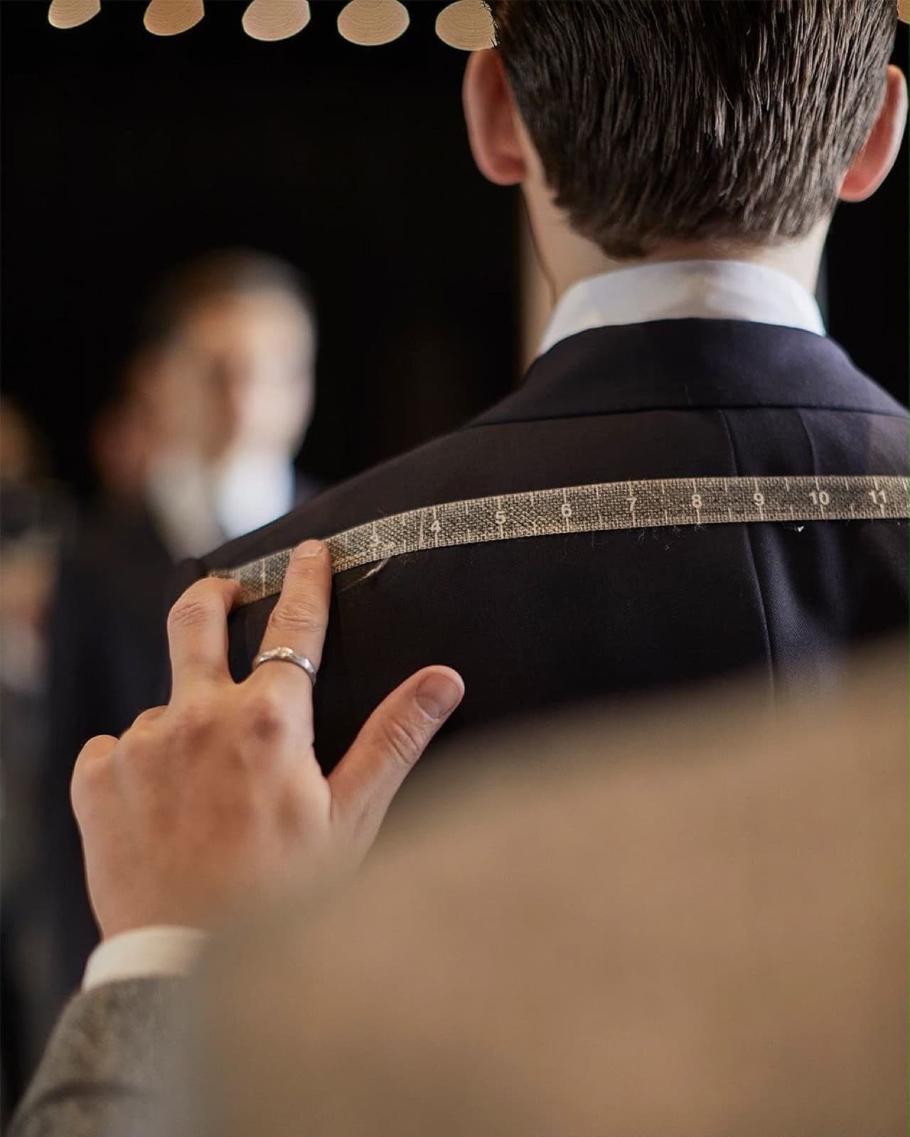 Tailor measuring a client's shoulder with a tape